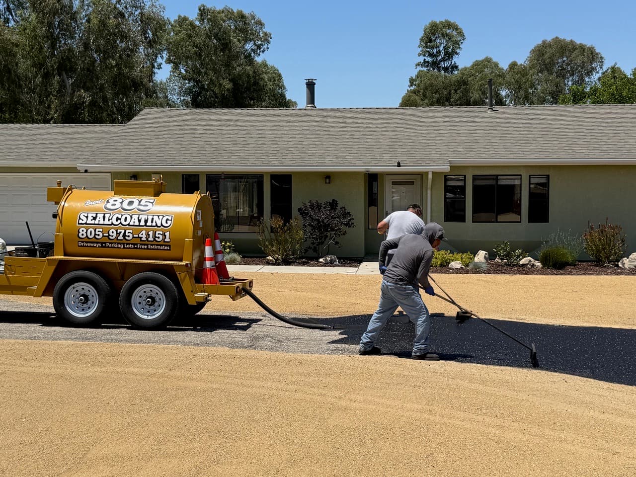 Two 805 Sealcoating crew members hand-applying and brooming fresh sealcoat across a residential driveway on the Central Coast