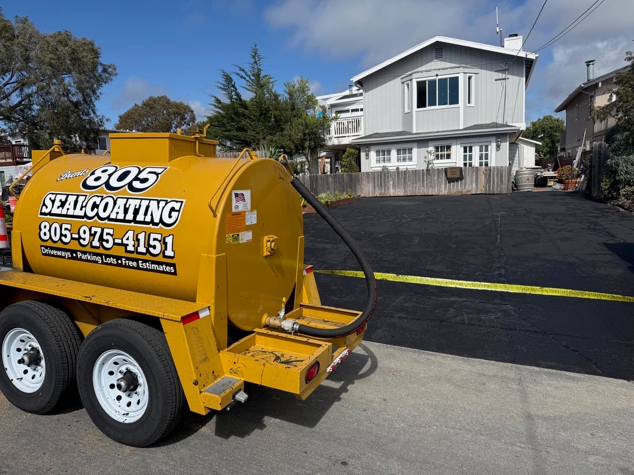 805 Sealcoating branded tank trailer beside a freshly sealed, deep-black residential driveway in Los Osos, California